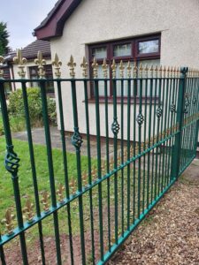 Black wrought iron fence panel with scroll detailing along a garden
